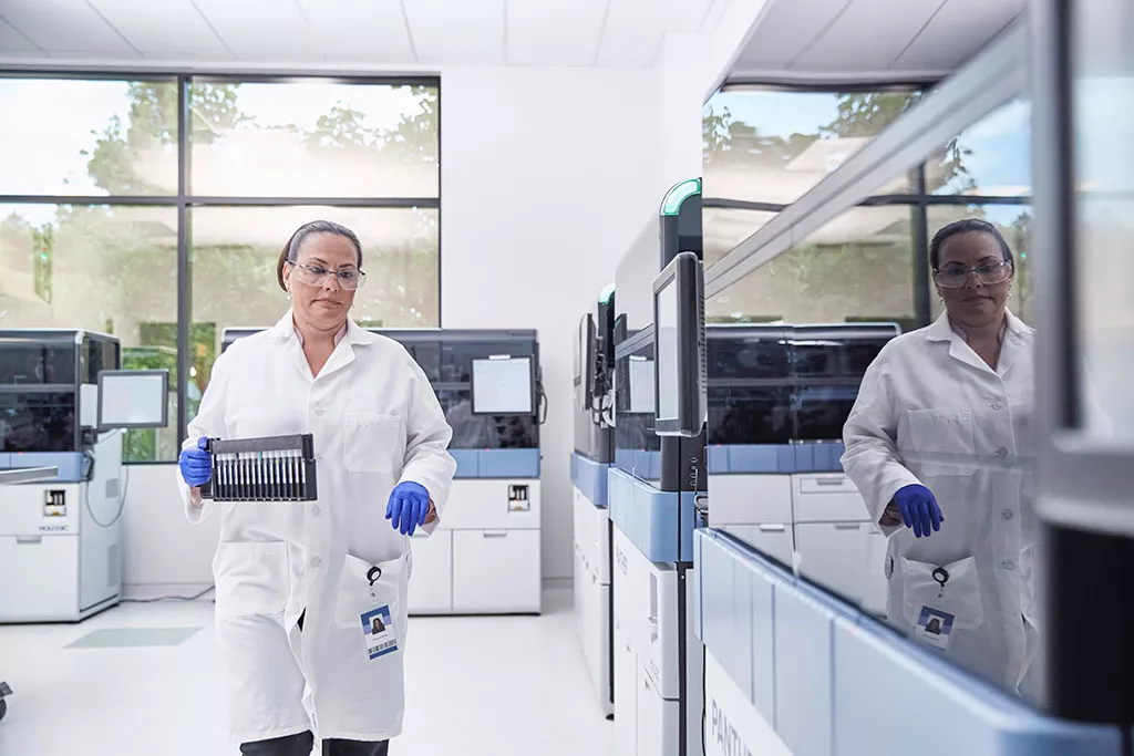 Lab technician carrying tray of vials in lab setting