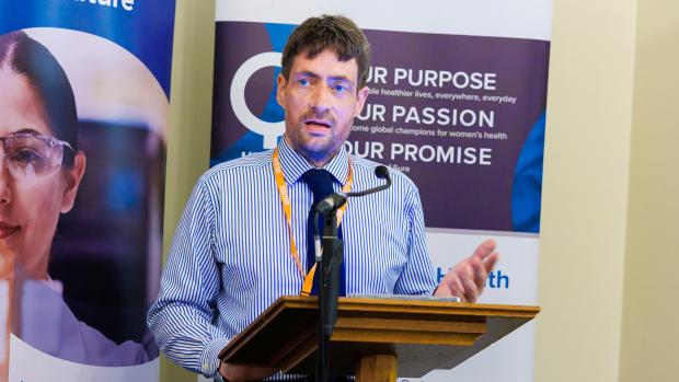 Man in stripe shirt giving speech infront of two vertical banners